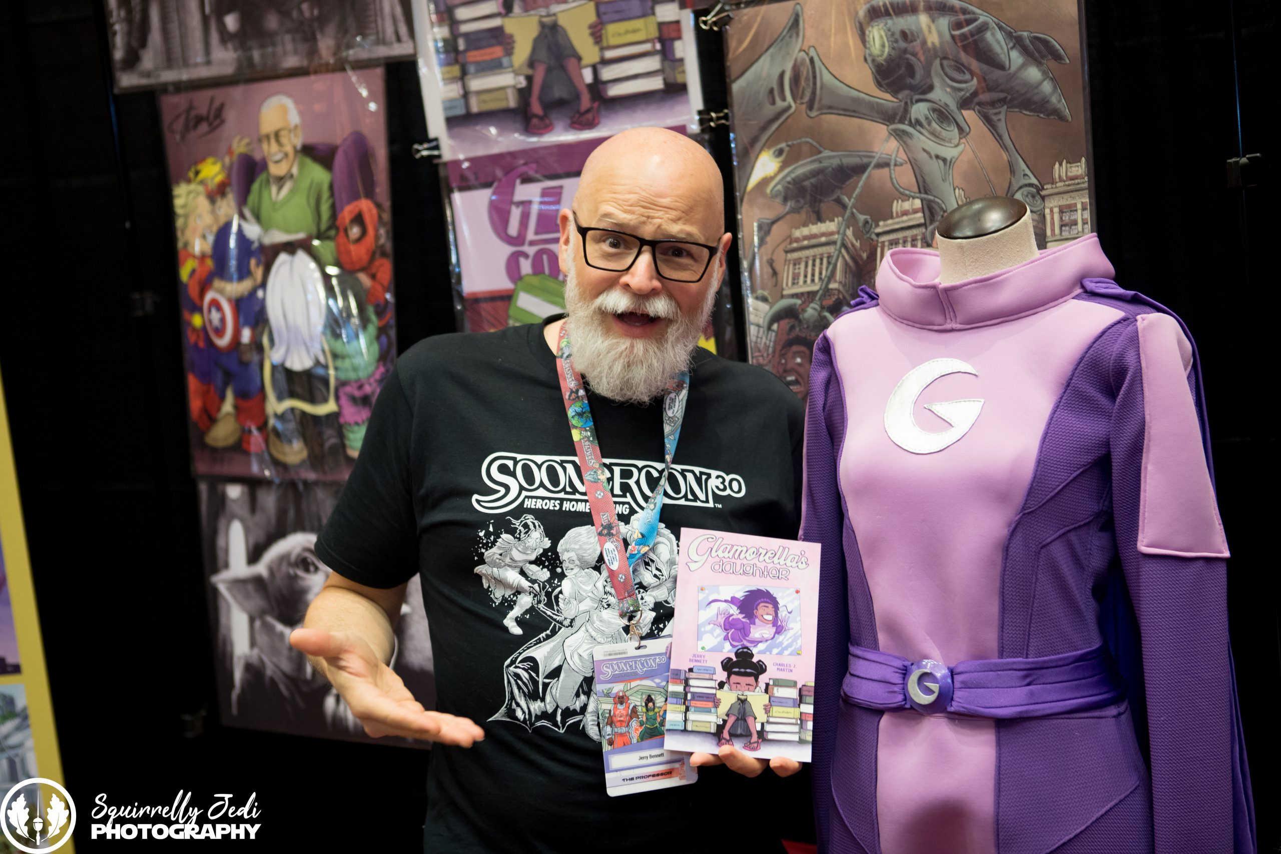 SoonerCon 30 Sunday-20 Artist Jerry Bennett gives a goofy style to the camera while holding his comic book Glamorella's Daughter and standing next to a Glamorella costume on a mannequin.