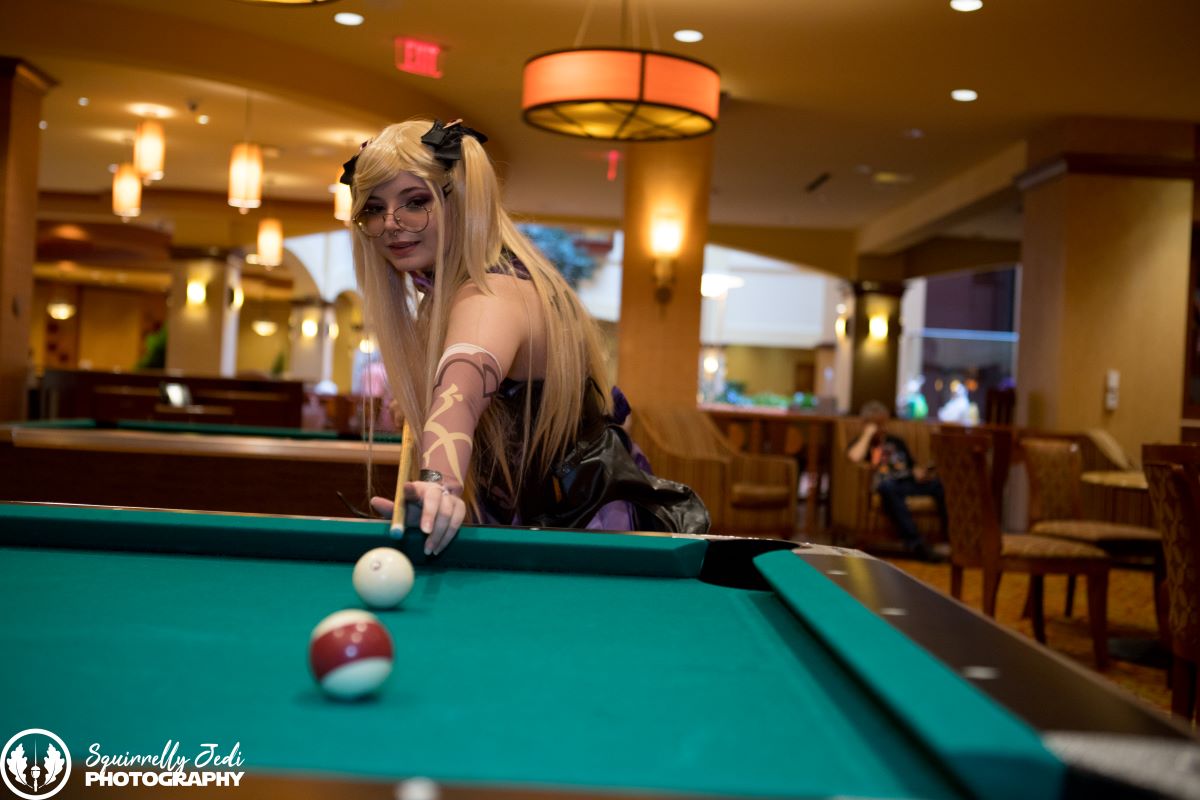 A cosplayer in a blonde wig lines up a shot on a pool table at the Embassy Suites hotel lounge area.