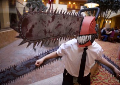 Chainsaw Man cosplayer poses for the camera with chainsaw head and arms.