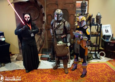 A Sith lord with red light saber poses with Din Djarin and another mandalorian. Grogu is in Din Djarin's satchel.