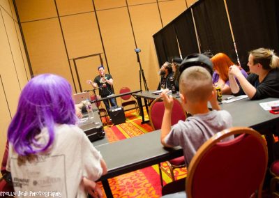 A class sits around a table while a speaker talks at the front with a microphone.